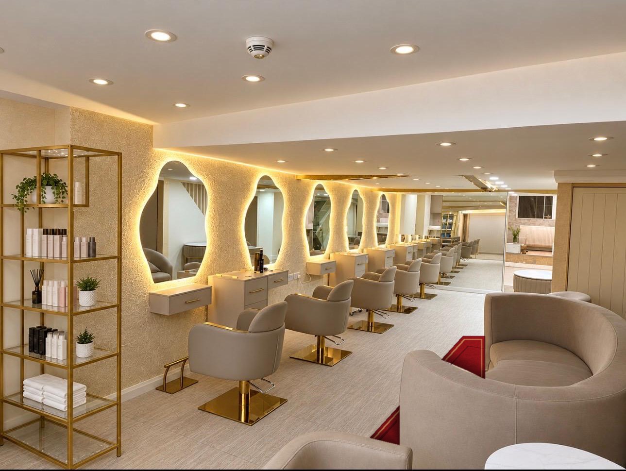 The salon floor: backlit cloud mirrors, beige chairs on gold bases and the waiting sofa on a red rug